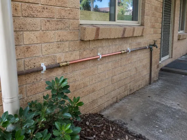 Repaired copper water pipe mounted on a brick exterior wall beside a window in Oatlands