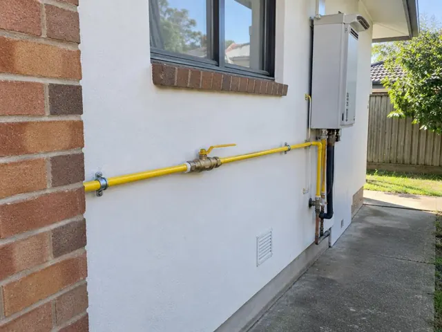 Yellow gas pipe and fittings on an exterior brick and rendered wall beside a hot water unit in Melrose Park