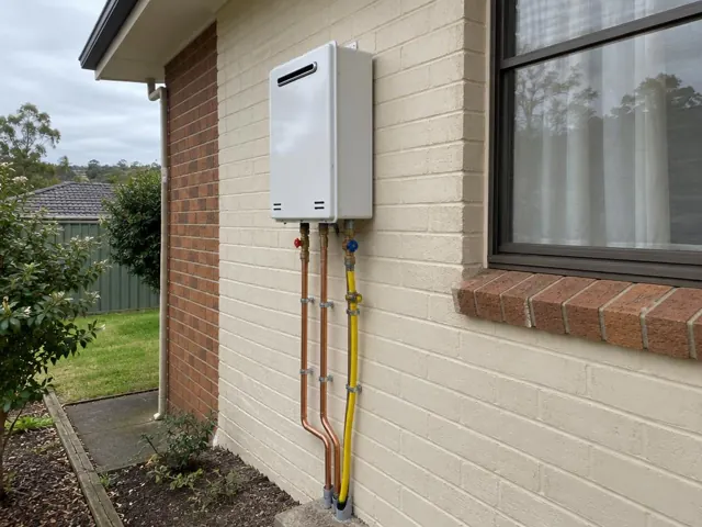Wall-mounted hot water unit on a brick house exterior beside a window and garden in Dundas Valley